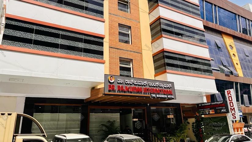 Exterior front view of Hotel Dr Rajkumar International with visible signage, parked vehicles and entrance.