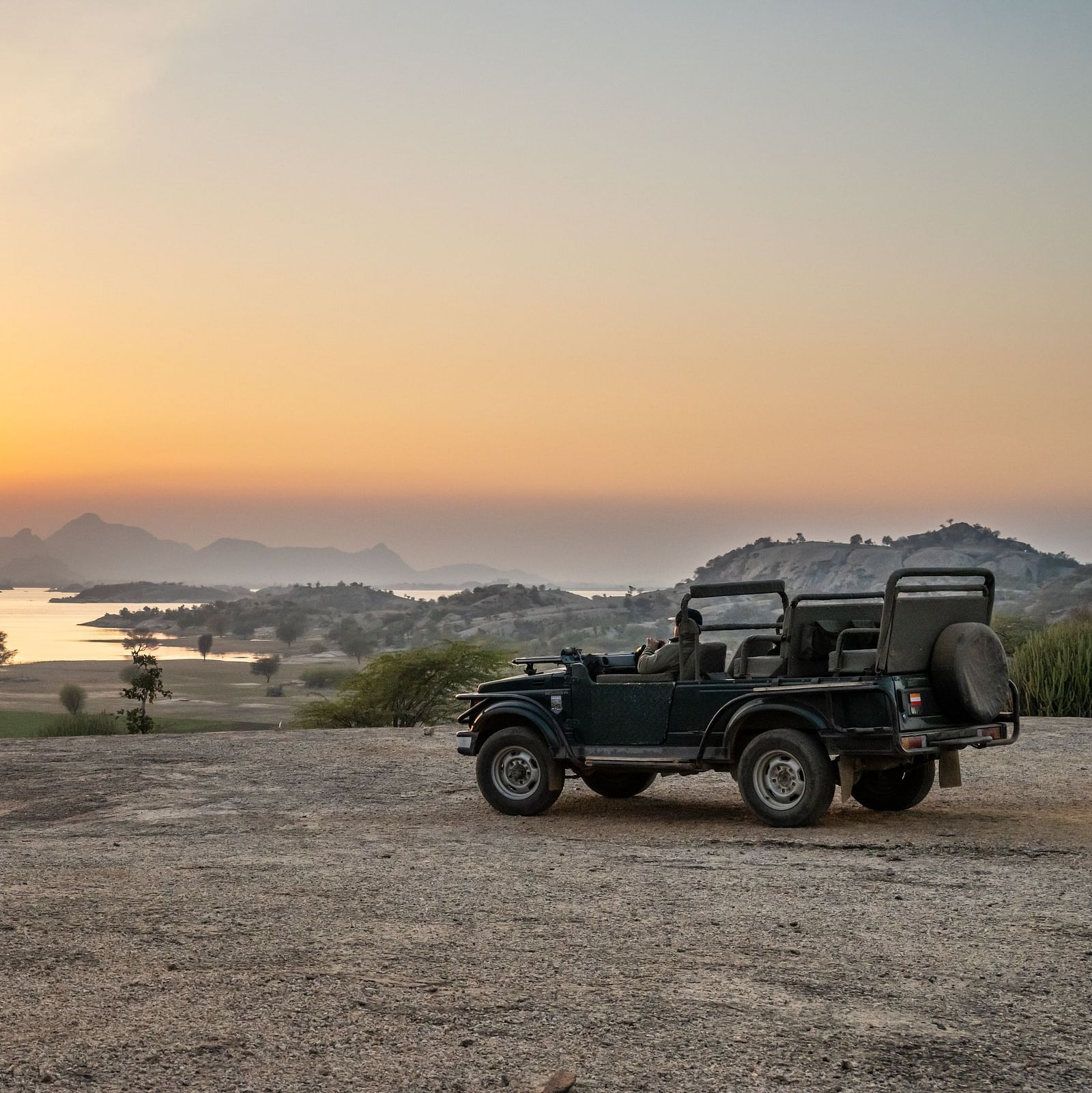 A jeep parked before a mountain with view of the sunrise at KURJA Jawai.