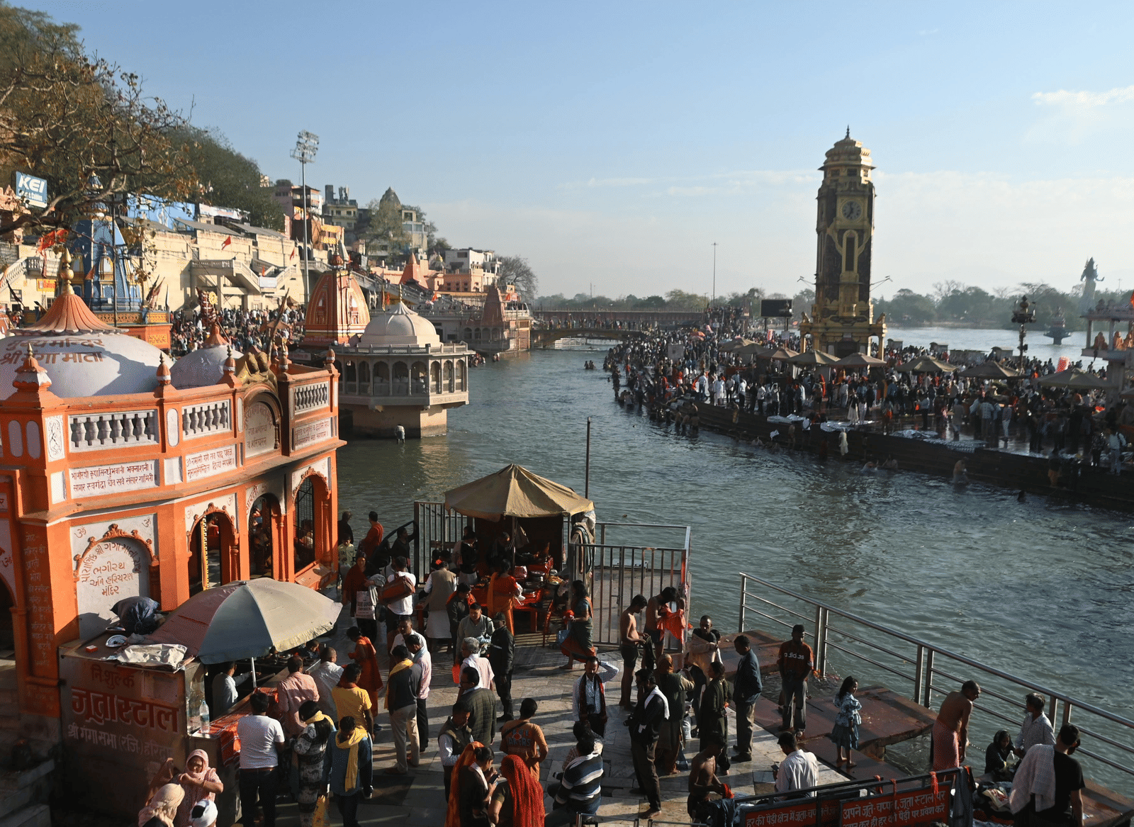 Several people scattered around on the banks of a river during the early morning, featuring a clock tower at a distance.