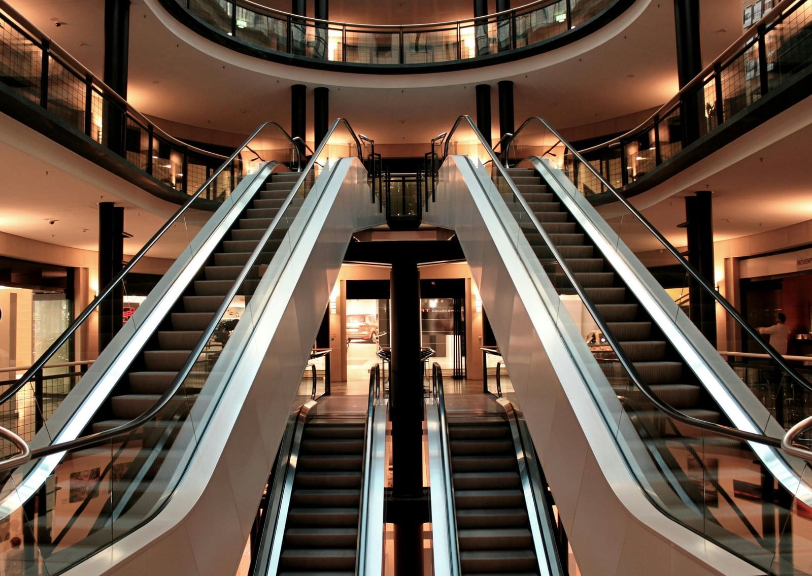 Twin escalators leading into a stylish shopping mall with bright lighting, glossy finishes, and multiple levels of retail stores.