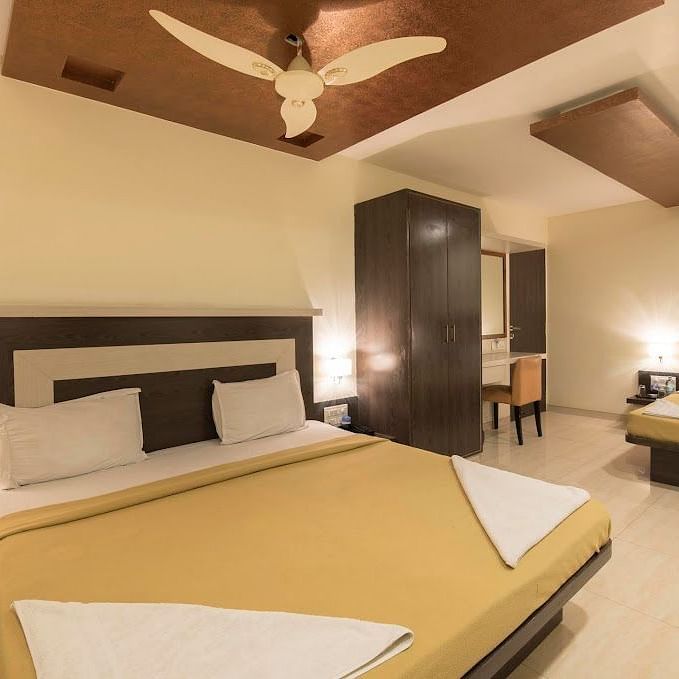 A room with two neatly made beds positioned a short distance apart, featuring a wardrobe, a vanity area, and a ceiling fan.