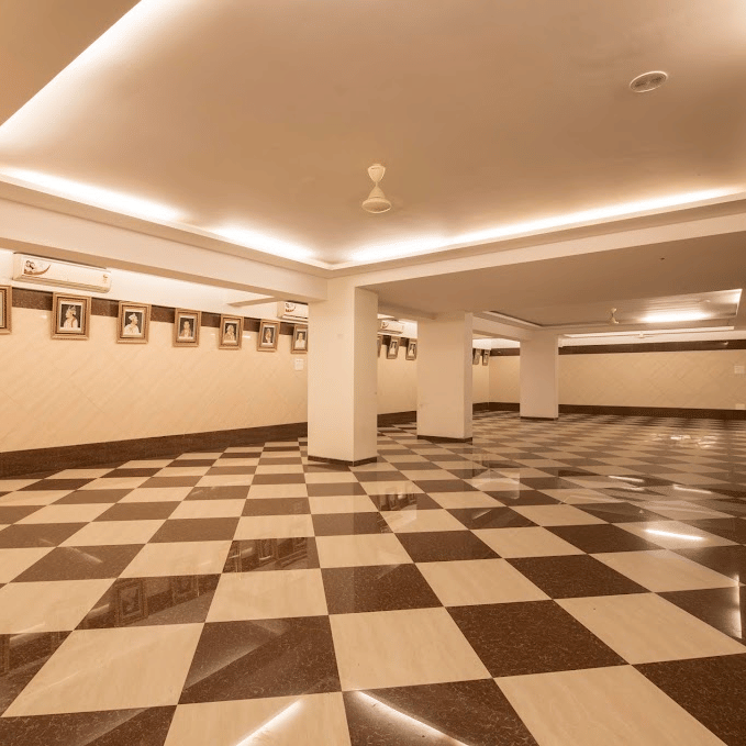 Long perspective of an empty function hall with recessed warm ceiling strip lights and checkered floor tiling.