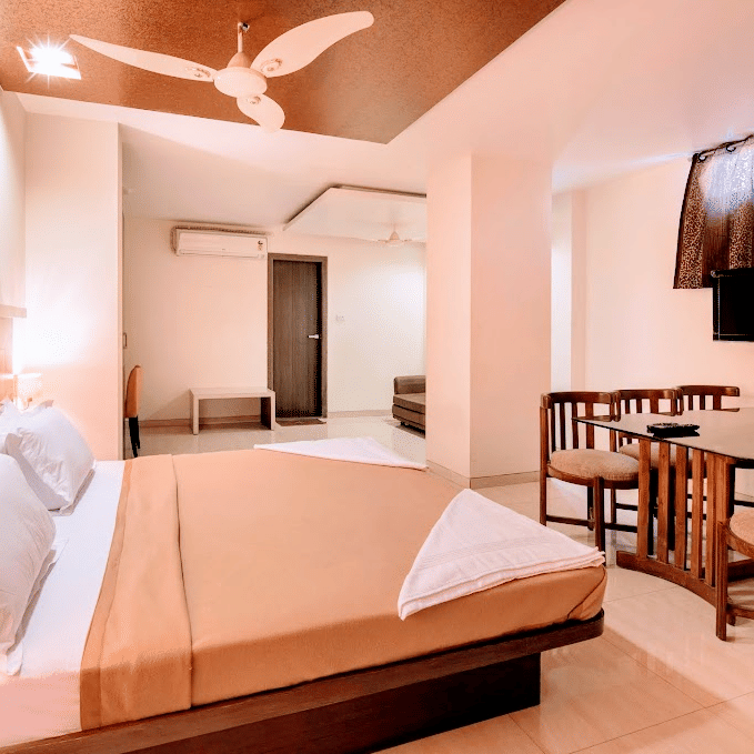 Suite room containing a double bed, small dining table with chairs, and wall-mounted television screen.