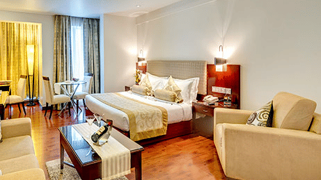 Wide view of a Premium Room at Hotel Hindusthan International Select Bengaluru with a king bed, cream sofas, wooden flooring, coffee table, and skylight.