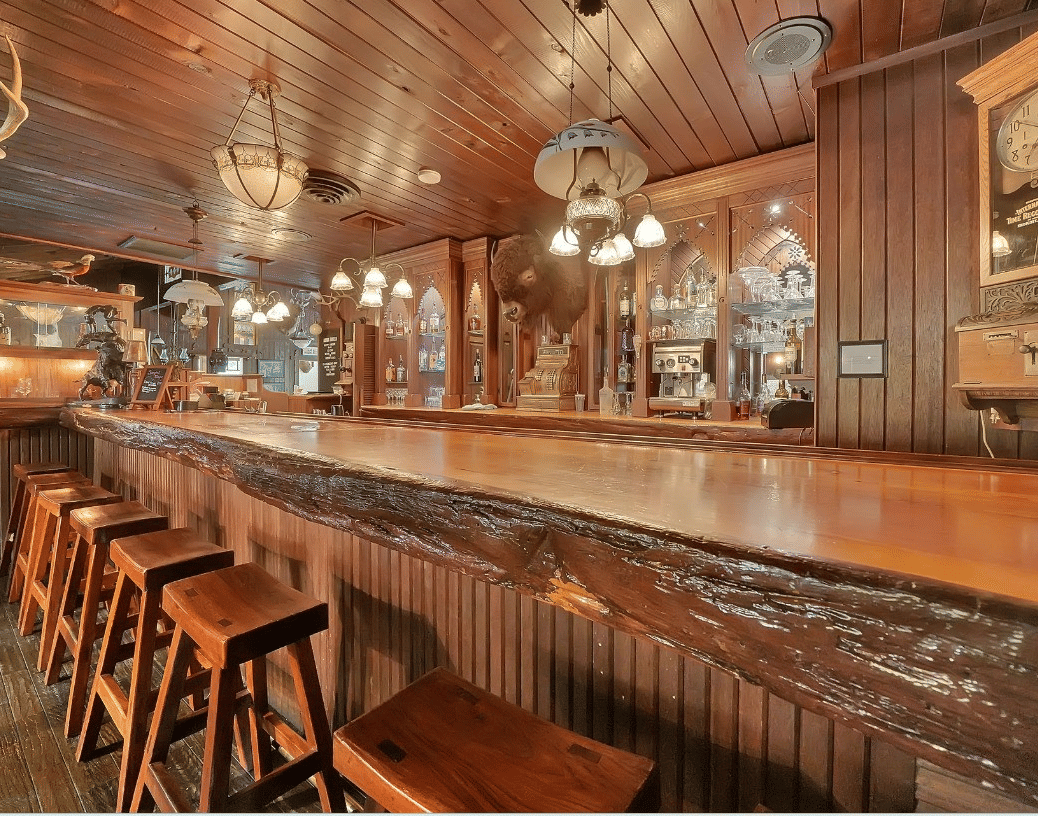 A warmly lit wooden bar at Shaver Lake Village Hotel with classic decor, vintage hanging lamps, and barstools lined along the counter.