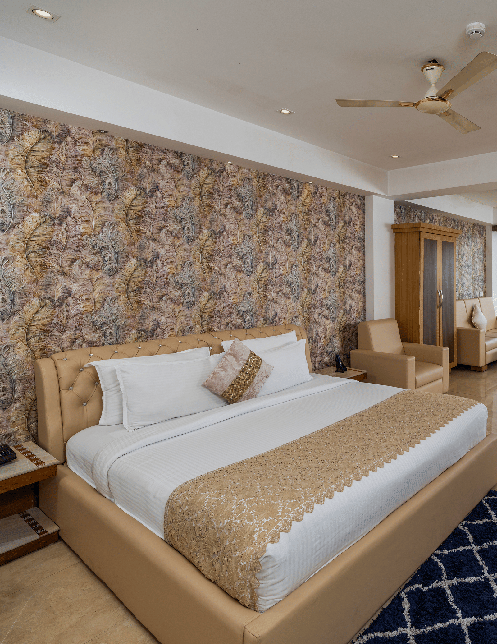 The bedroom of the 90-Degree Club Suite at Parakkat Nature Hotel and Resorts, Munnar, featuring a large bed, a stone-patterned accent wall, a ceiling fan, and glass windows.