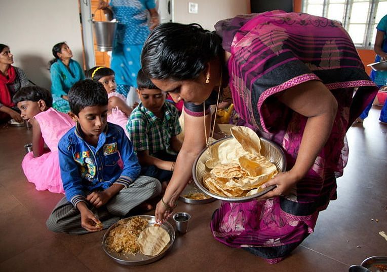 People eating from plates on the floor, indoor setting - Shreyas Retreat