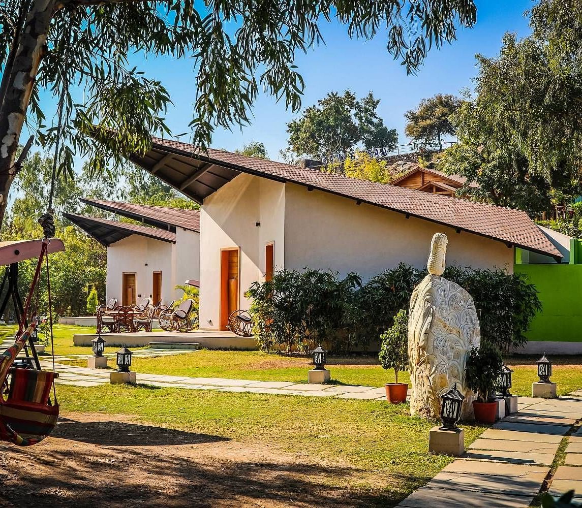 A modern building with a sloping roof sits amidst lush greenery.- Bamboo Saa Resort & Spa, Udaipur