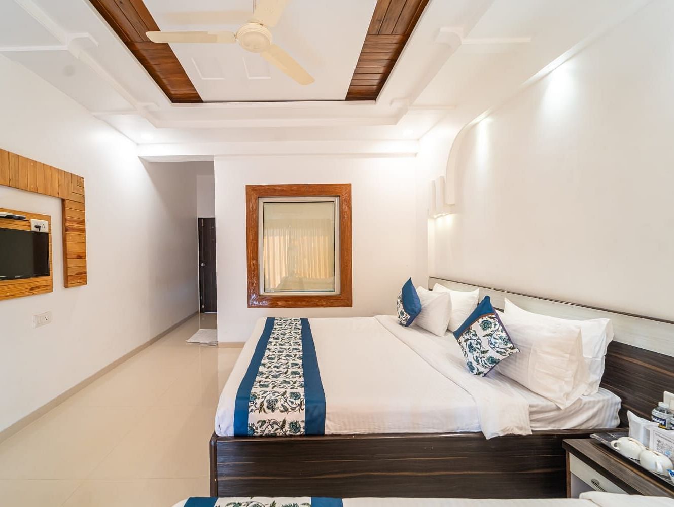 Deluxe Valley View Room featuring a bed with white and blue linens, a dark wood headboard, a side table, and a wall-mounted television, with neutral-toned walls and ceiling
