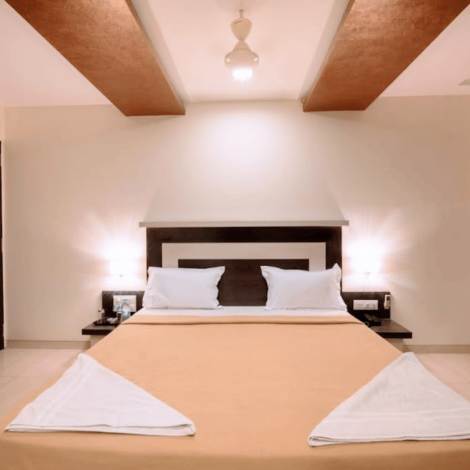 front view  of a modern hotel double bed with cream-colored bedding and decorative folded towels.