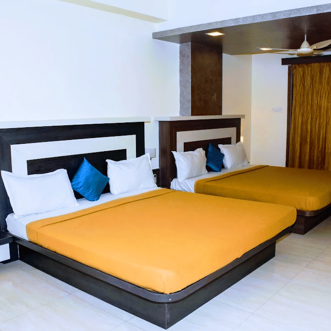 Spacious family room layout with two queen beds featuring bright orange linens and blue accent pillows.