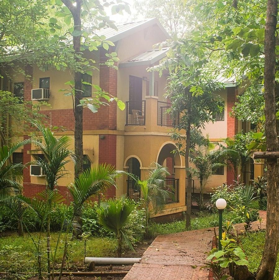 Classic Room Exterior - Sajan - two storied yellow ochre coloured building with a brown pathway leading upto it lined by white globe lights.