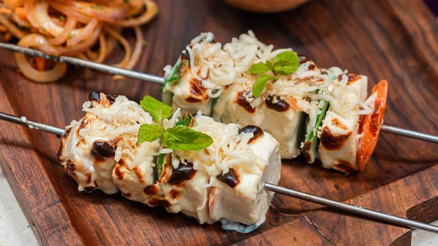 A wooden plate serving chicken and veggies on a stick, accompanied by a side of sauce and onions at Crescent Spa & Resort, Indore