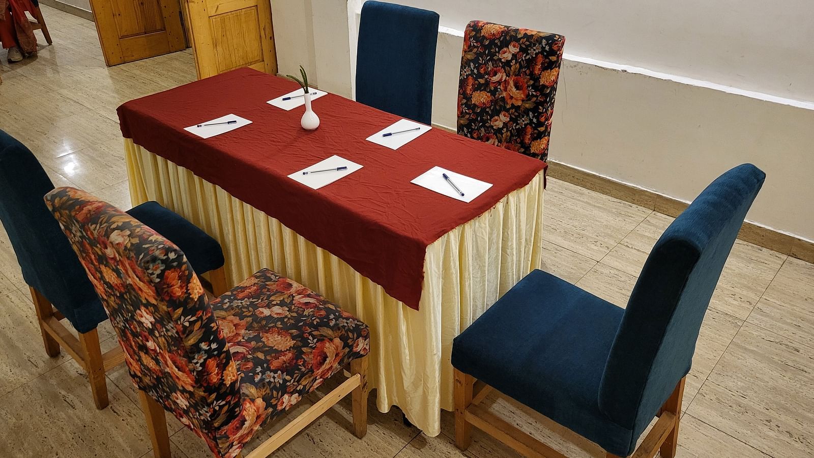 A meeting setup with a table covered in red and gold fabric, surrounded by floral-patterned chairs in a well-lit room at Dagshai Manor Kasauli - Inde Hotels.