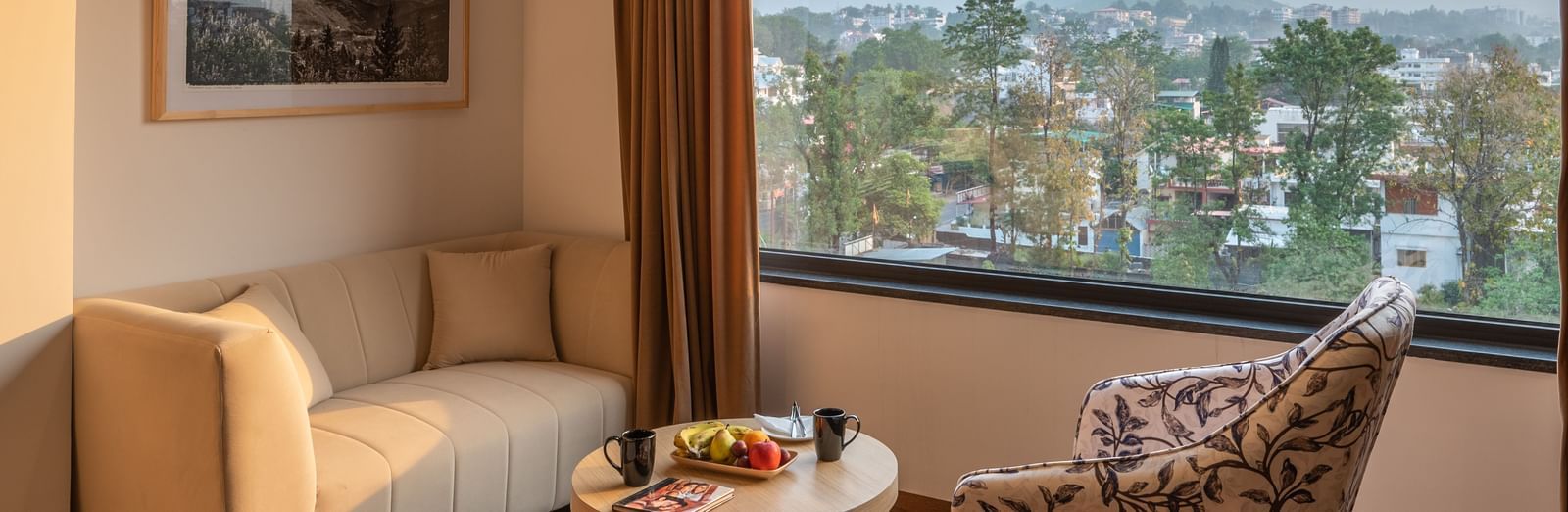 Living area of the lavish suites in Dehradun at Vishranti Hotel featuring a large window, a sofa, chair and a round table.