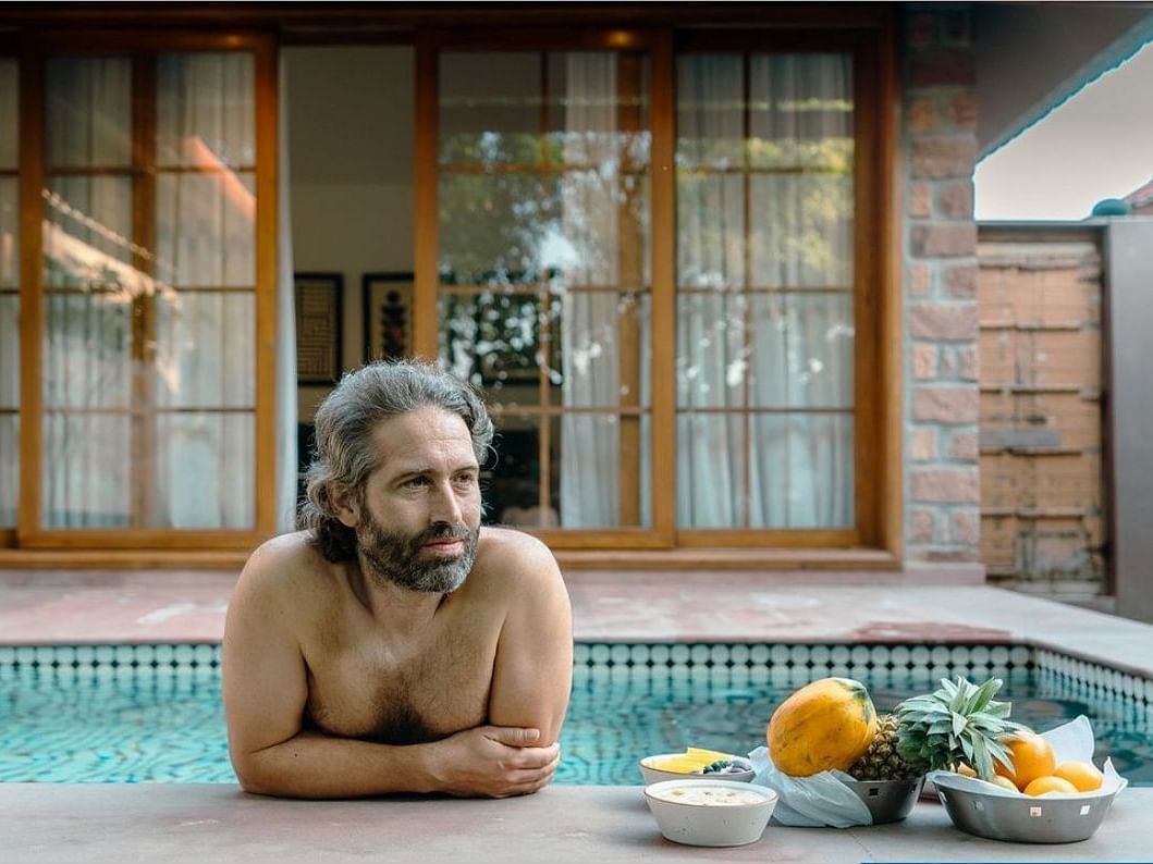 A man standing on a swimming pool with an assortment of fruits on the side at Surpura Bagh.