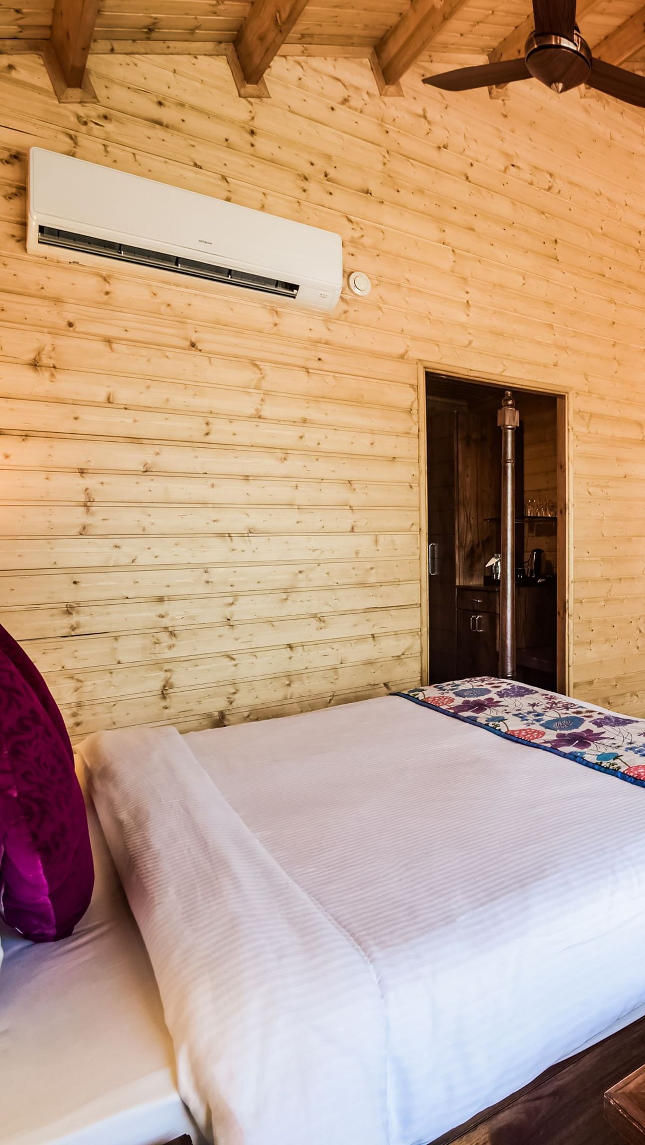 A cosy room with wood-paneled walls, a bed, a mounted TV, and an air conditioner.- Bamboo Saa Resort & Spa, Udaipur