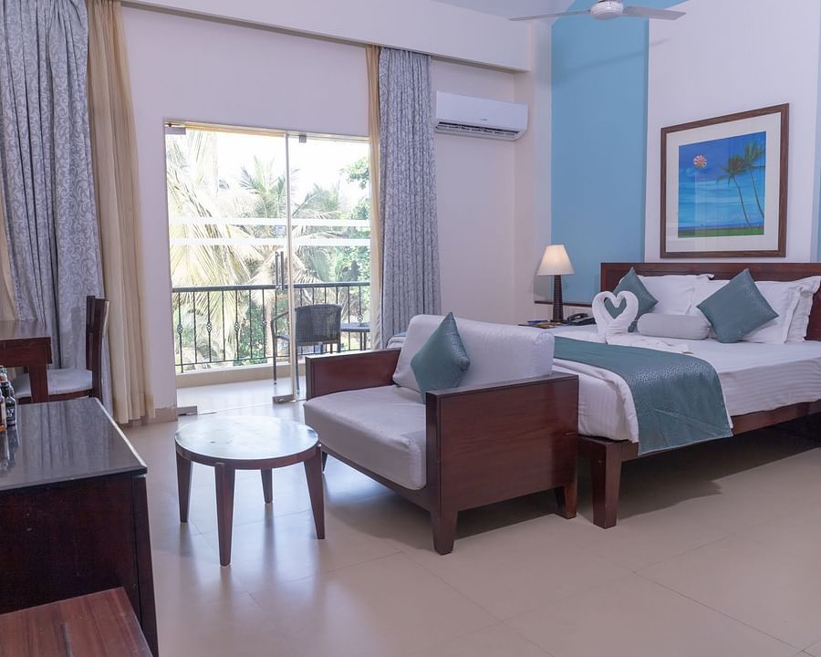 Complete view of the Deluxe room with a double bed, a couch a small tea table and a balcony at Kyriad Prestige Calangute, Goa