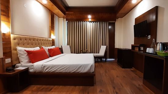 An image of a bedroom featuring a double size bed, a flat TV screen, a cabinet for storing things and a seating area at one corner - Mastiff Xanadu, Manali