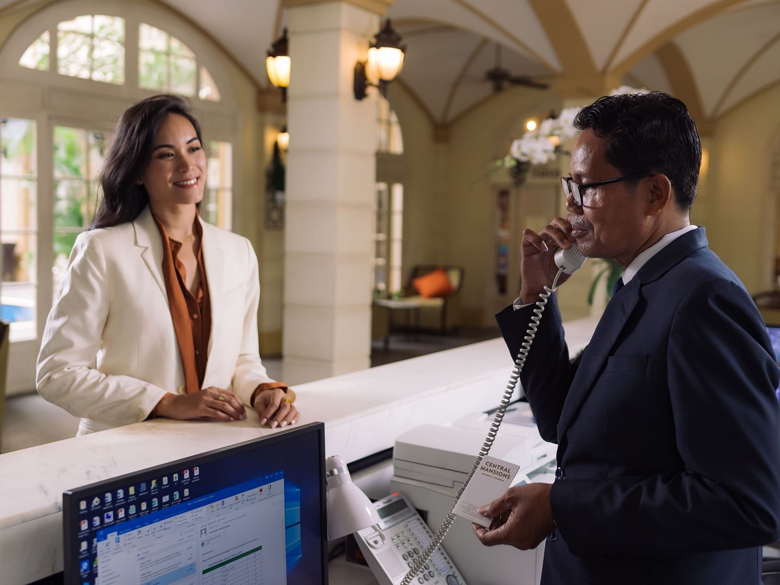 A hotelier on a call while the woman is standing near the reception desk | Central Mansions, Phnom Penh