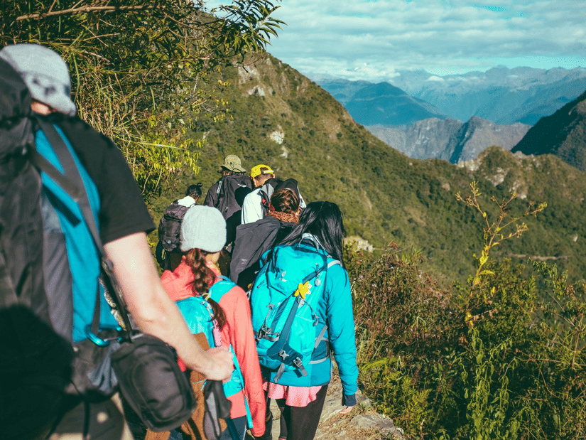 A group of people trekking on a pathway leading to a mountainous range with spiky hills in the background.