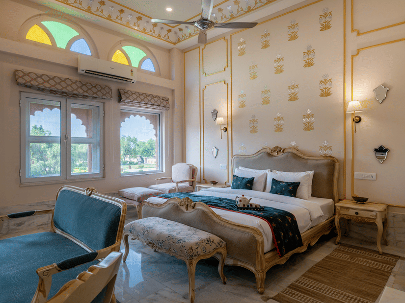 The elegant Maharaja Suite at Umaid Palace, luxury rooms near Delhi, featuring a king-size bed, futons, sofa, lamps, and side tables, and offering traditional decor.