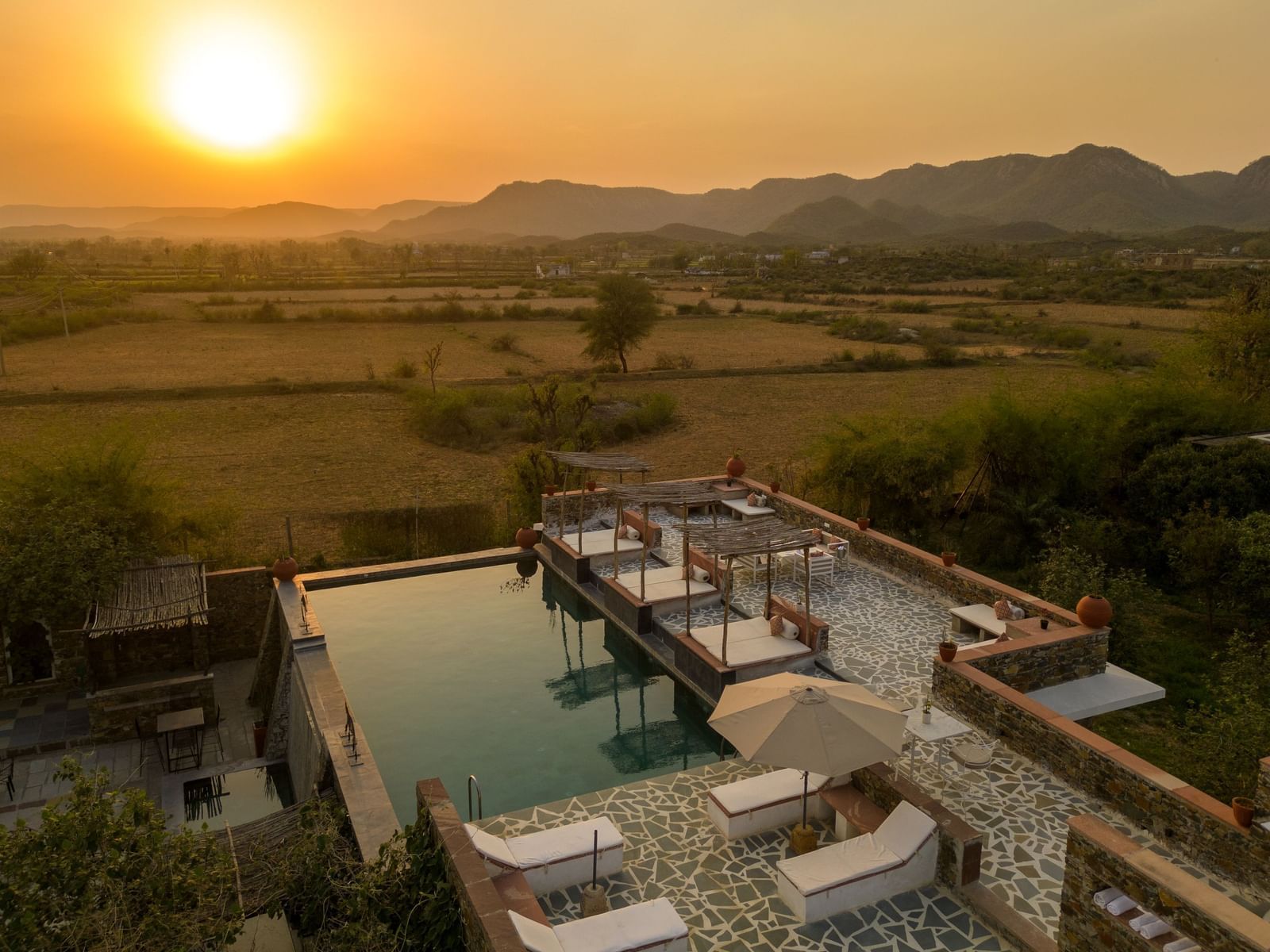 A serene sunset seen in the shot with a roof top swimming poll below it - Utsav Camp Sariska