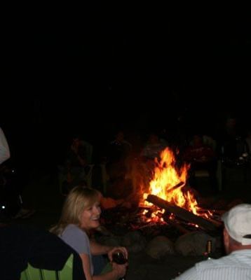A campfire event at Kit Carson Lodge & Restaurant shows two people sitting near a fire at night. 
