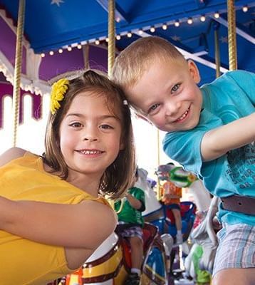 Two young children smile while riding a carousel at an amusement park.