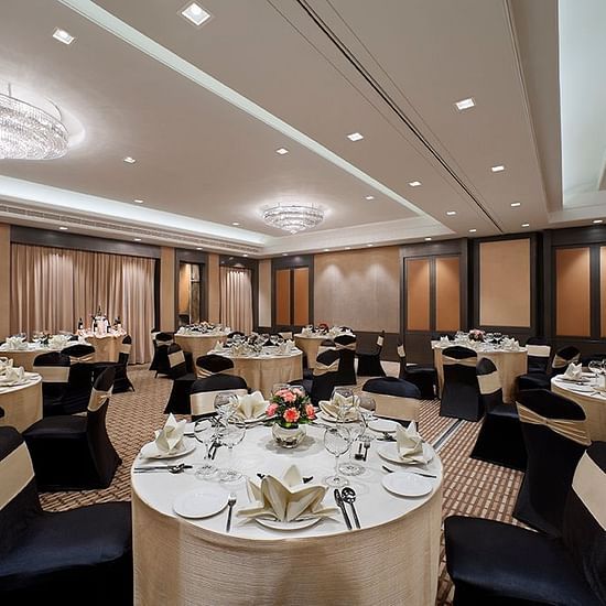 Banquet hall with round tables set for a formal event, featuring chandeliers and high ceilings.