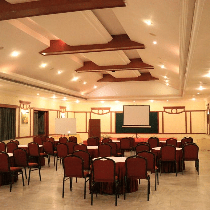 Indoor banquet hall with round tables and red chairs arranged for an event, featuring modern ceiling lights and decor - Black Thunder, Coimbatore