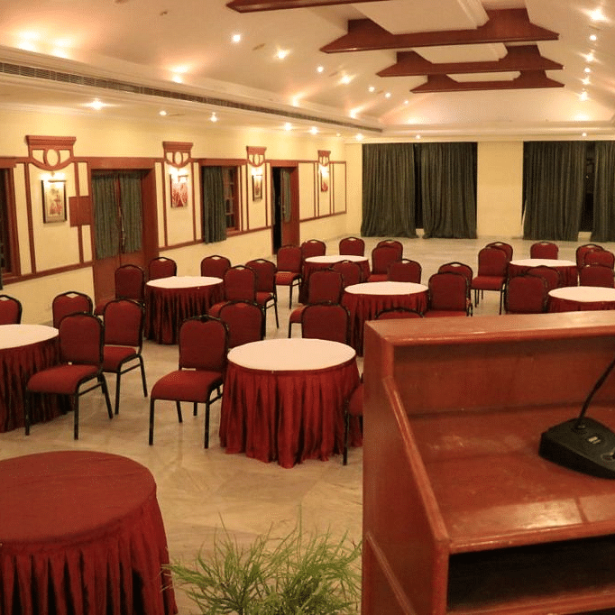 Modern indoor conference room with round tables and chairs arranged for meetings or events, complete with a podium and stage - Black Thunder, Coimbatore