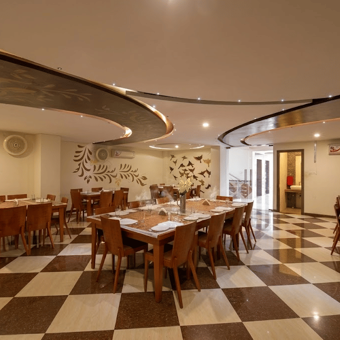 Wide angle view of a dining hall with checkered tile floors, multiple wooden tables, and structured curved ceilings.