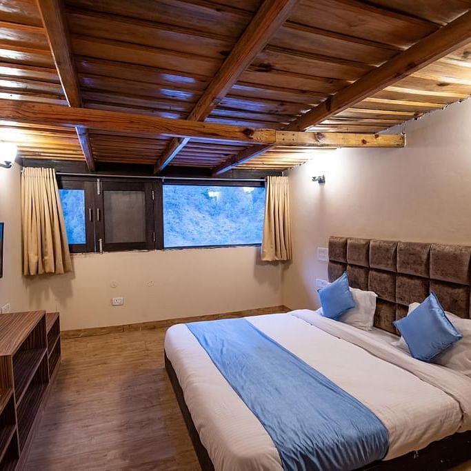 A wooden-ceiling bedroom with a double bed, window view, and TV