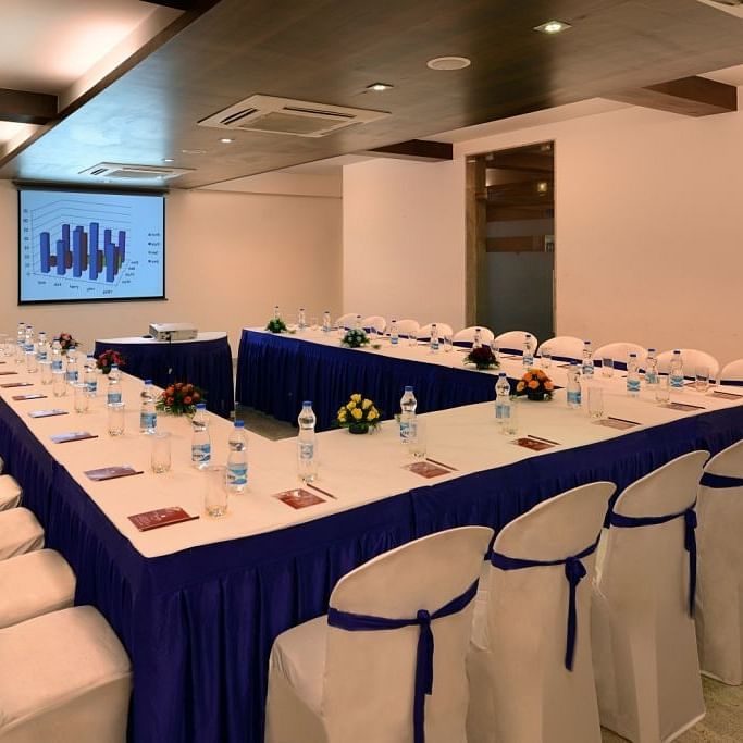 A conference room at the Dwarkadhish Lords Eco Inn set up with a U-shaped table, chairs, and a projection screen.