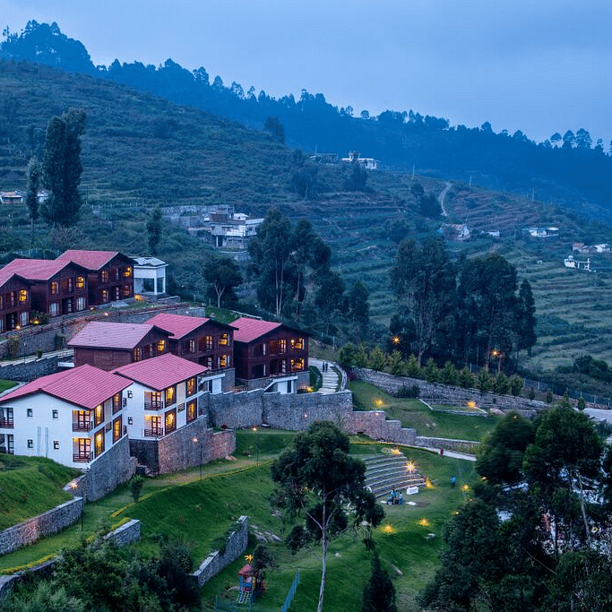 A drone shot of the GReaT Trails Kodaikanal By GRT Hotels property surrounded by lush greenery and trees with a clear sky
