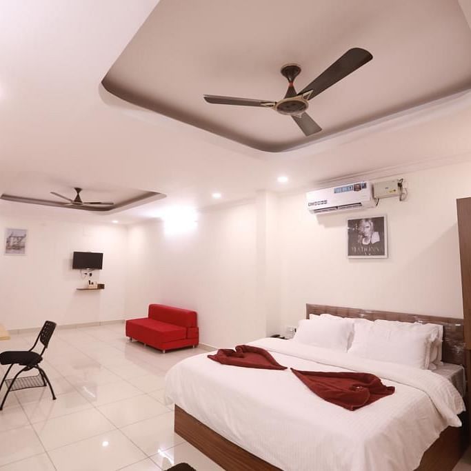 Large suite with a red sofa, a plush bed, a work desk, and  a chair | Vistar Resort, Bengaluru