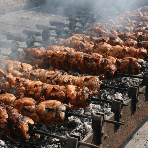 Numerous metal skewers with meat lined on ignited charcoal grill in the process of making kababs.