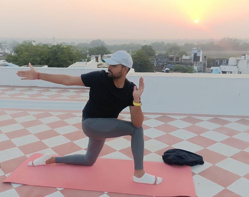 A person performs a yoga pose on a mat on a rooftop with a sunrise or sunset in the background.