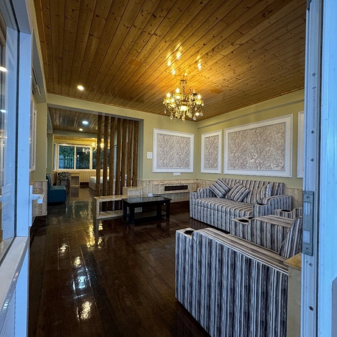 An image of a seating room which has a seating area like sofa, centre table. Chandelier hung from a wooden ceiling - Avianna Group of Hotels & Resorts