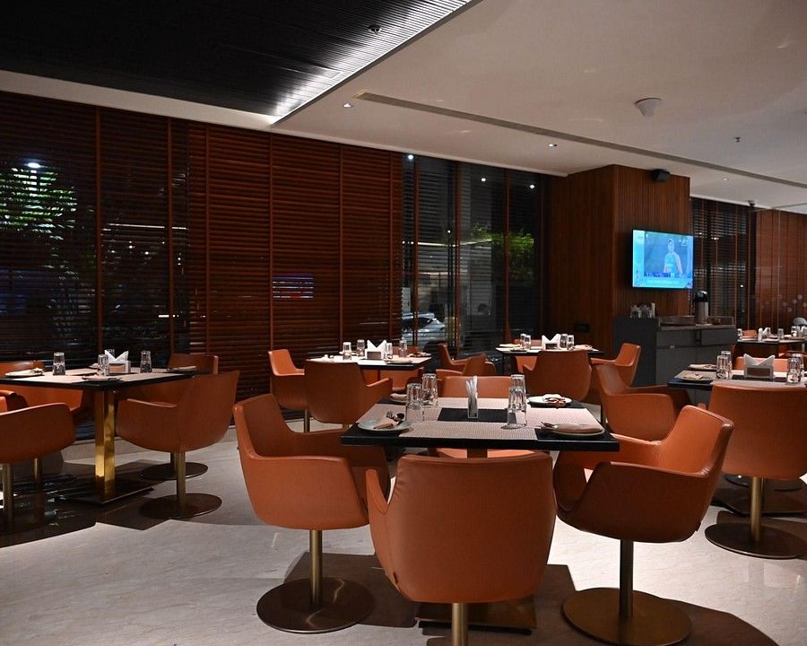 A contemporary dining area with round tables and orange chairs set against a warm, wooden backdrop.