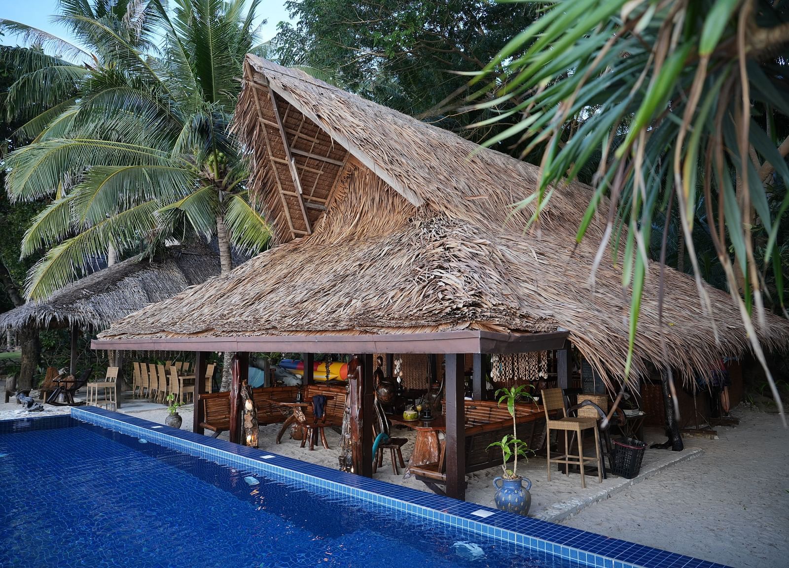 Exterior view of the thatched-roof restaurant beside the pool at Flower Island Resort.