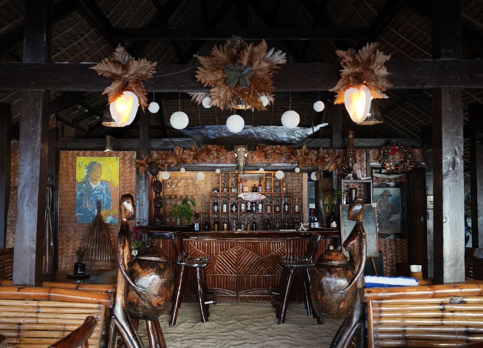 Wood and bamboo bar counter with stools and hanging decor at Flower Island Resort.