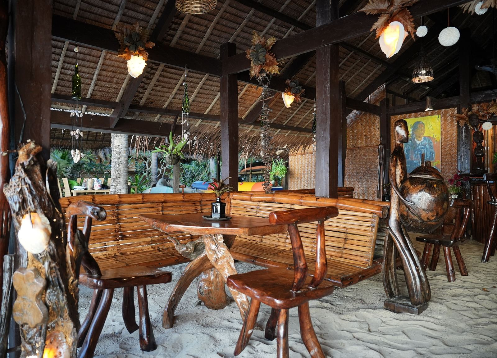 Wooden dining setup under thatched roof with bamboo furniture at Flower Island Resort.
