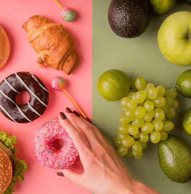A top down view of processed food placed on a pink backdrop on the left and fruits placed on a sage green backdrop on the right