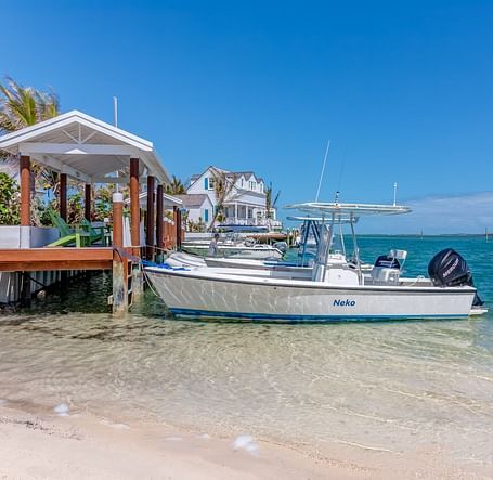 Boat docked at a shore with houses and palm trees | Abaco Inn