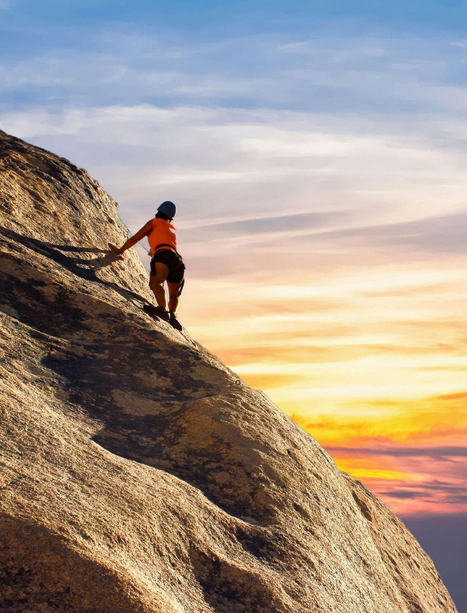 A rock climber looking at the sunset hues in the sky from the top of a mountain.