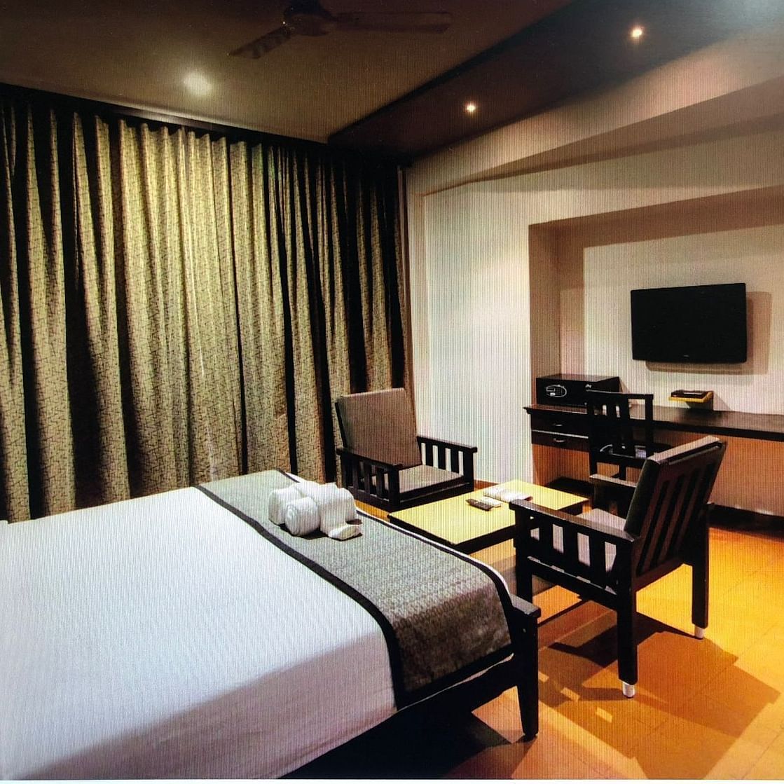 A king size bed facing the TV and a small sitting space at Damanganga Valley Resorts