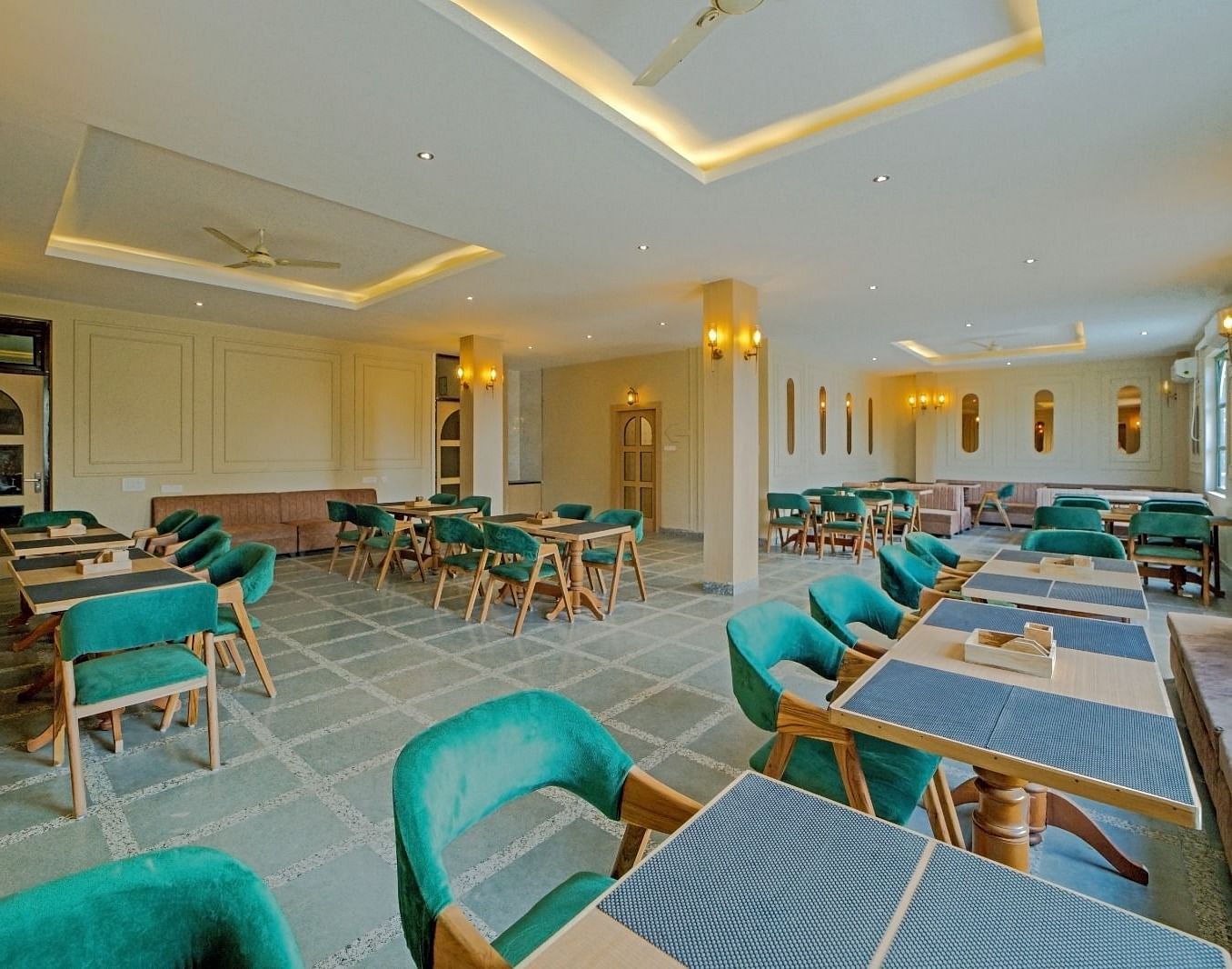 Elegant dining area at Grassfield Riveria Resort, Jaipur, with teal upholstered chairs, wooden tables, and warm lighting.