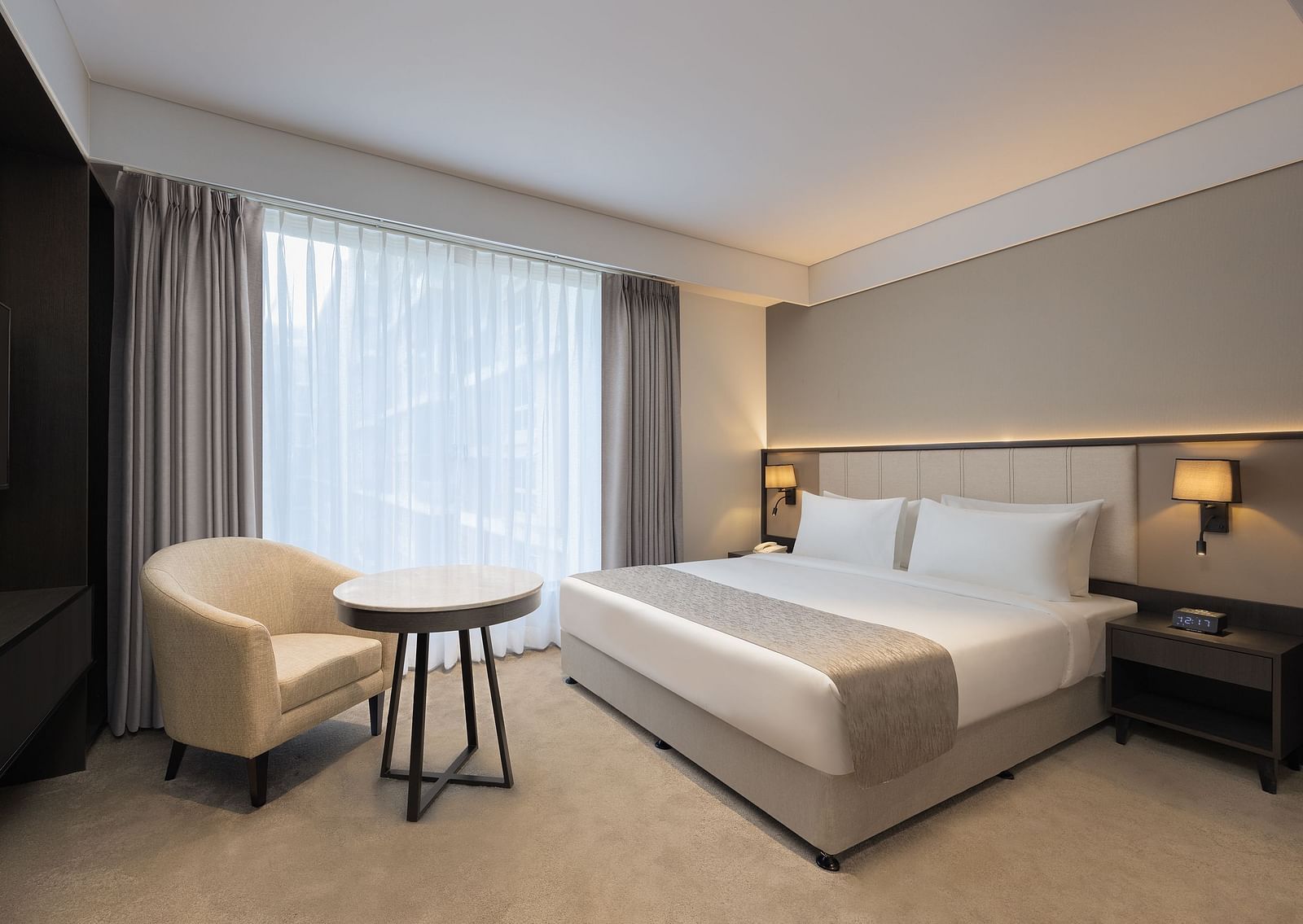 Deluxe King Room with a king size bed and a comfortable chair beside a large window at Essentia Premiere, Pune. 